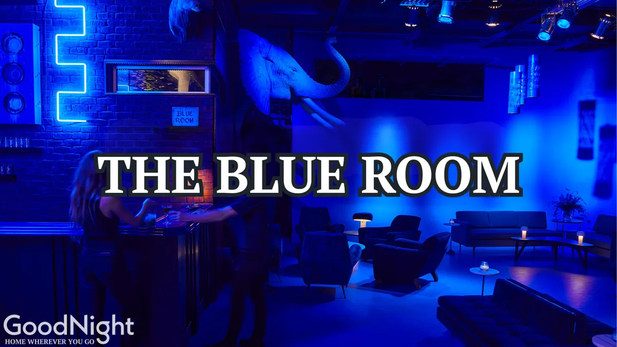 A stylish, modern community lounge with neon lighting, a striking blue color scheme, and unique wall decor. The space is designed for intimate conversations and casual relaxation, offering guests a sophisticated spot to unwind or connect with fellow travelers.
