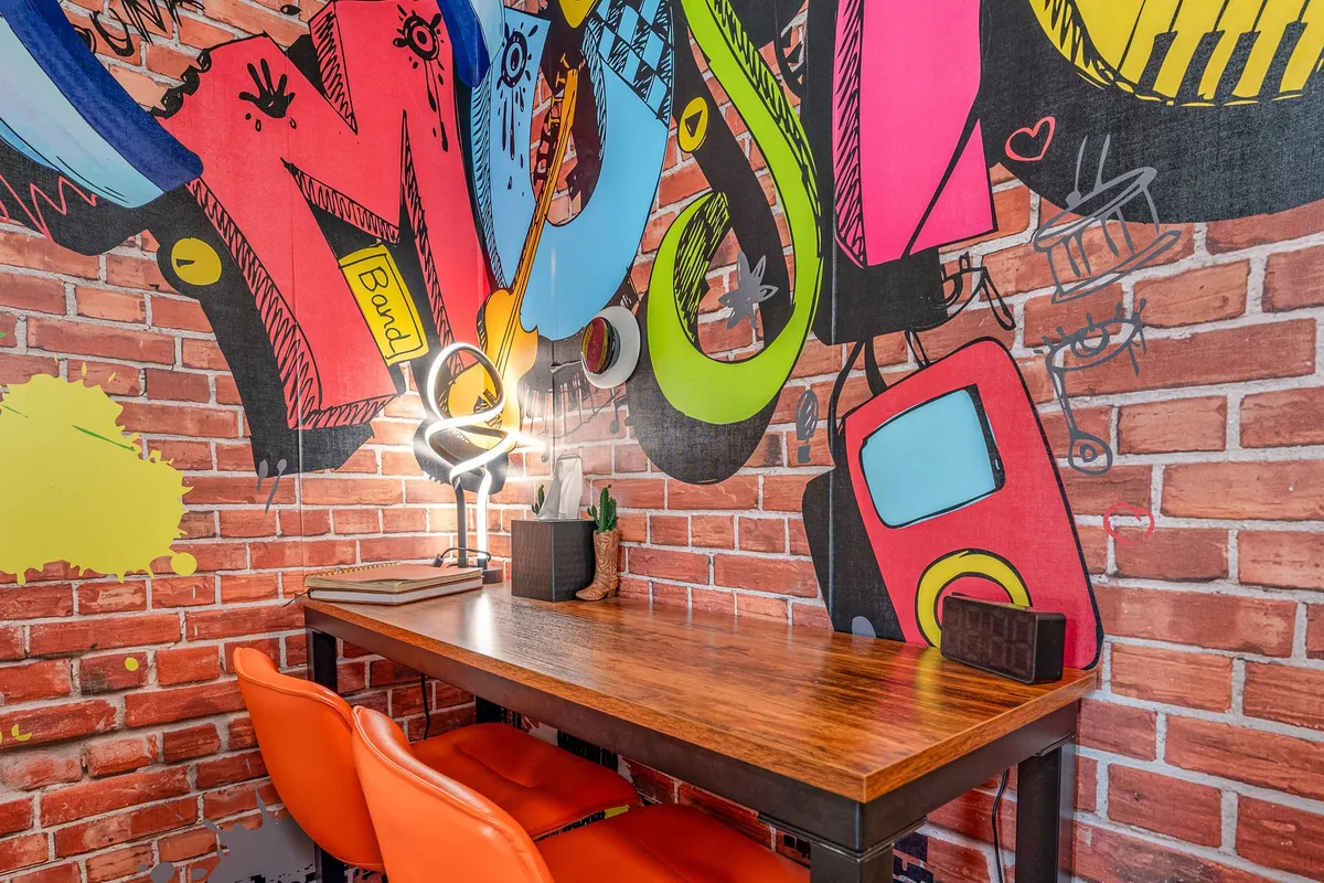 This image features a vibrant workspace with a colorful graffiti wall, a wooden desk, orange chairs, and a desk lamp. The setting is energetic and inspiring, ideal for creative brainstorming or productivity.