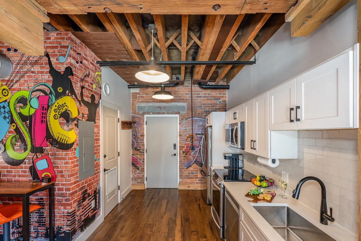 A close-up perspective of a kitchen island with a colorful mural backdrop, modern stainless steel appliances, and bright, inviting lighting. The image emphasizes the kitchen’s functionality and the inspiring environment for meal preparation or group dining.