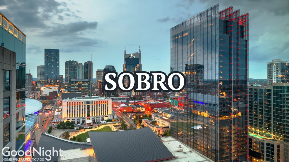 A sweeping view of the Nashville city skyline at dusk, with illuminated buildings and the glowing SOBRO sign. The scene captures the downtown’s vibrant nightlife, setting the scene for exploration and discovery in the city’s musical core.